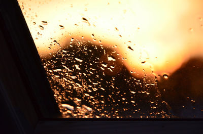 Close-up of wet window against sky during sunset