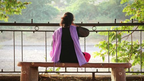 Rear view of woman sitting on railing against trees