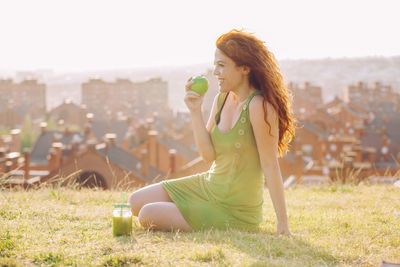 Young woman drinking while sitting on field