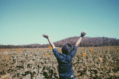 Woman with arms raised standing on field against clear sky