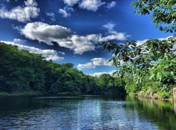 Calm lake surrounded by trees against cloudy sky