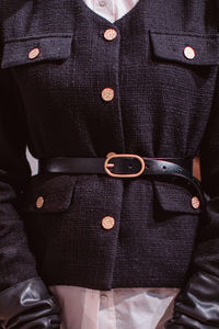 Fashion details of a classy black jacket, leather belt and golden buttons.