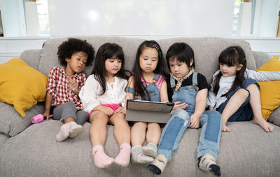 High angle view of friends sitting with digital tablet on sofa