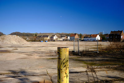 Road by buildings against clear blue sky