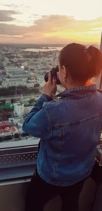 Man photographing with cityscape against sky during sunset