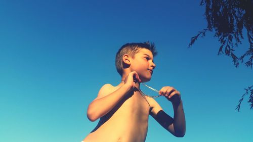Low angle view of shirtless boy against clear blue sky