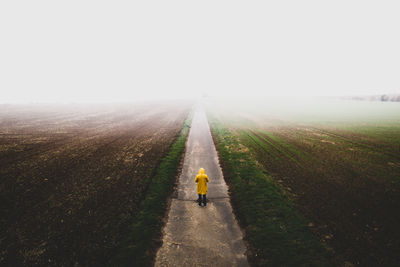 Rear view of person on road amidst field against sky