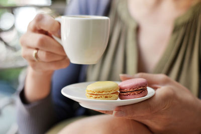 Cropped image of woman holding coffee cup with macaroons in saucer