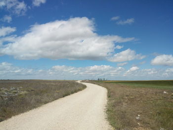 Road passing through field against cloudy sky