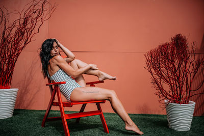 Woman sitting on chair against wall