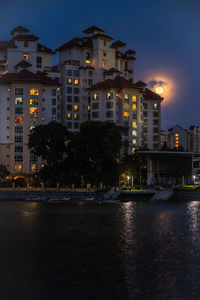 Illuminated buildings by river against sky at night