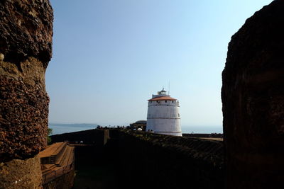 Lighthouse amidst buildings against clear blue sky