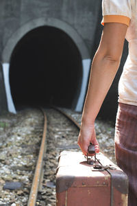 Midsection of woman with suitcase standing on railroad track