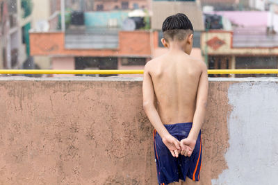 Rear view of shirtless boy standing against wall