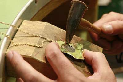 Cropped hands of person using hammer on necklace