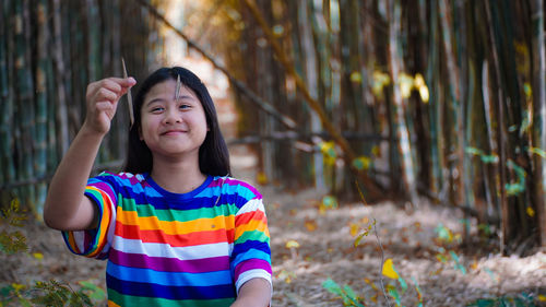 Smiling girl holding dry leaf in forest