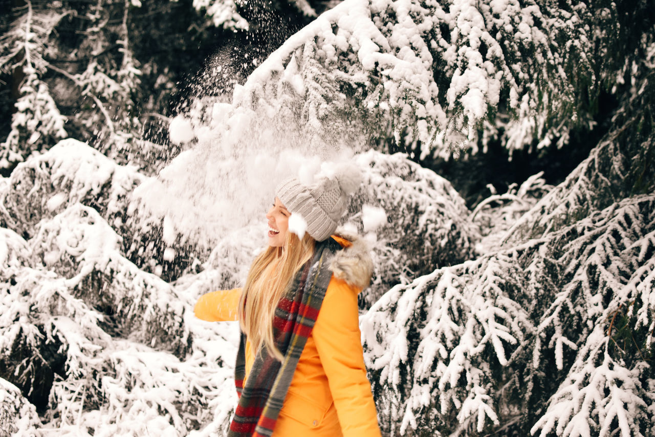 WOMAN STANDING ON SNOW COVERED TREE