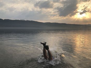 Man swimming in sea against sky during sunset