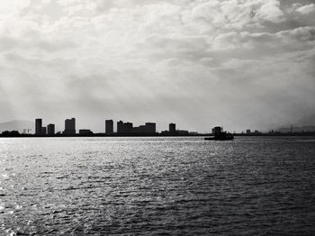 Silhouette buildings by sea against sky