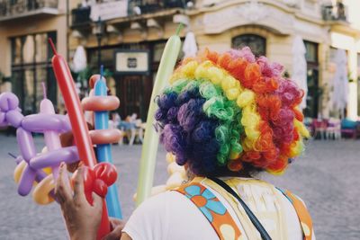 Rear view of clown holding balloons in city