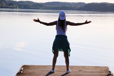 Rear view of woman with arms outstretched standing by lake
