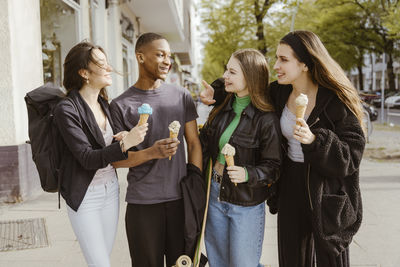 Happy young friends eating ice creams at sidewalk