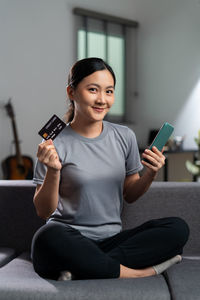 Portrait of young woman using mobile phone while sitting on sofa at home