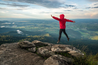 Rear view of woman jumping on rock against sky