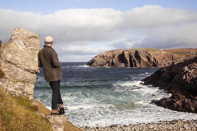 Man standing on rock by sea against sky