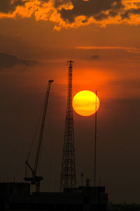 Silhouette cranes against orange sky