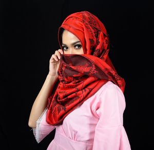 Portrait of young woman standing against black background