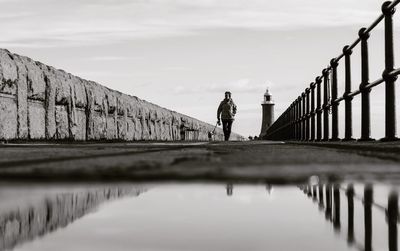 Man standing on footbridge over sea against sky