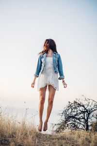 Rear view of young woman walking on field against clear sky