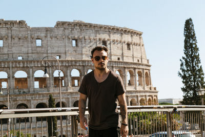Portrait of young man wearing sunglasses while standing against coliseum