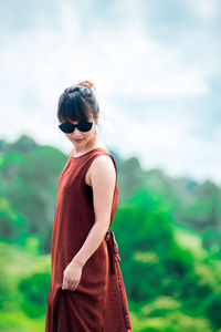 Side view of young woman wearing sunglasses standing on mountain against cloudy sky