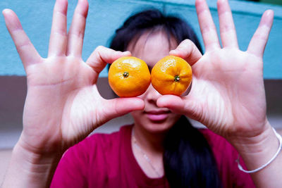 Close-up of woman holding orange over eyes