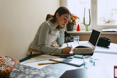 Young woman doing homework while writing in book at home