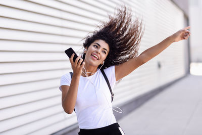 Happy woman listening music while dancing by wall in city