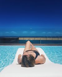 Woman lying by swimming pool against sea