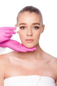 Cropped hands of doctor giving beauty treatment to young woman against white background