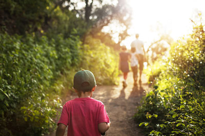 Rear view of boy walking with family on road amidst trees on sunny day