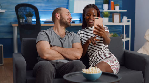 Smiling couple doing selfie sitting on sofa at home