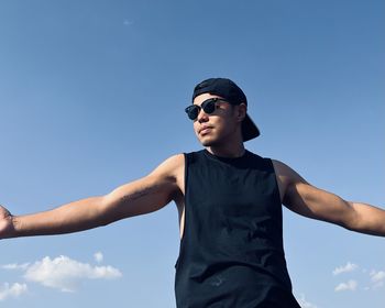 Low angle view of young man standing against blue sky