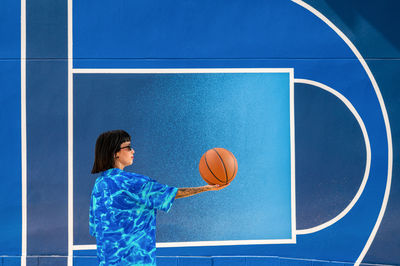 Caucasian girl with sunglasses and tattoos on a blue background with a basketball