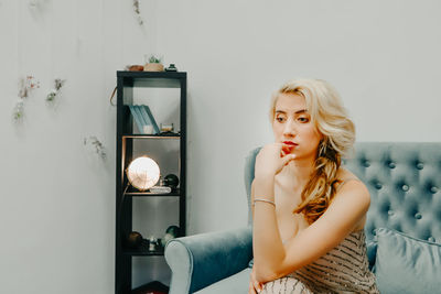 Young woman looking away while sitting on wall at home