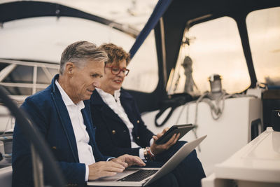 Senior couple using technologies while traveling in yacht during sunset