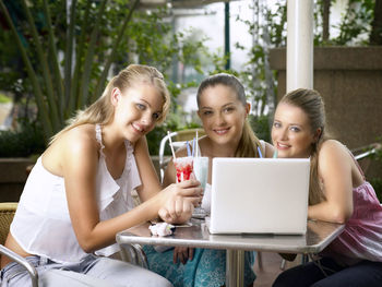 Portrait of smiling friends sitting with desserts and laptop at restaurant