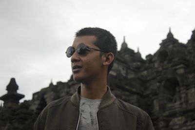 Young man wearing sunglasses looking away while standing against temple