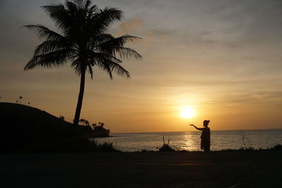 Silhouette man standing on beach against sky during sunset