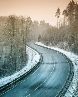 Snow covered road by trees against sky